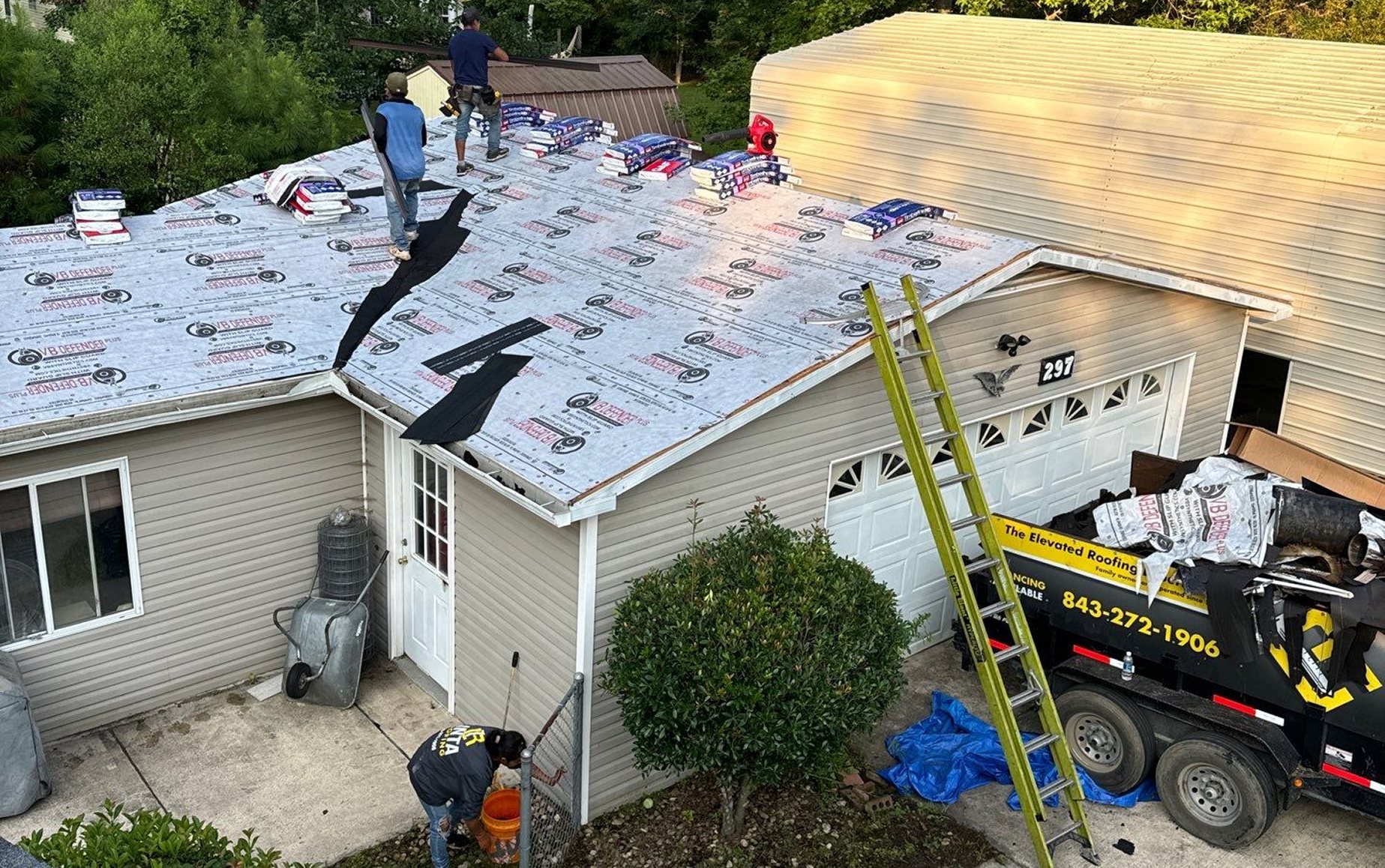 Linta Roofing crew laying shingle bundles over new synthetic underlayment, with a Linta dump trailer in the driveway