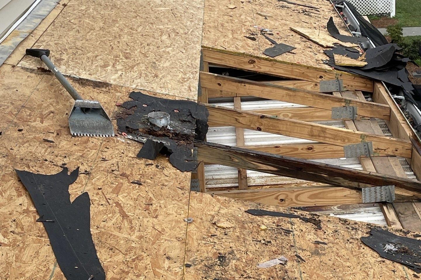 Roof decking exposed during a tear-off, with a shingle removal shovel next to rotted wood around a vent pipe