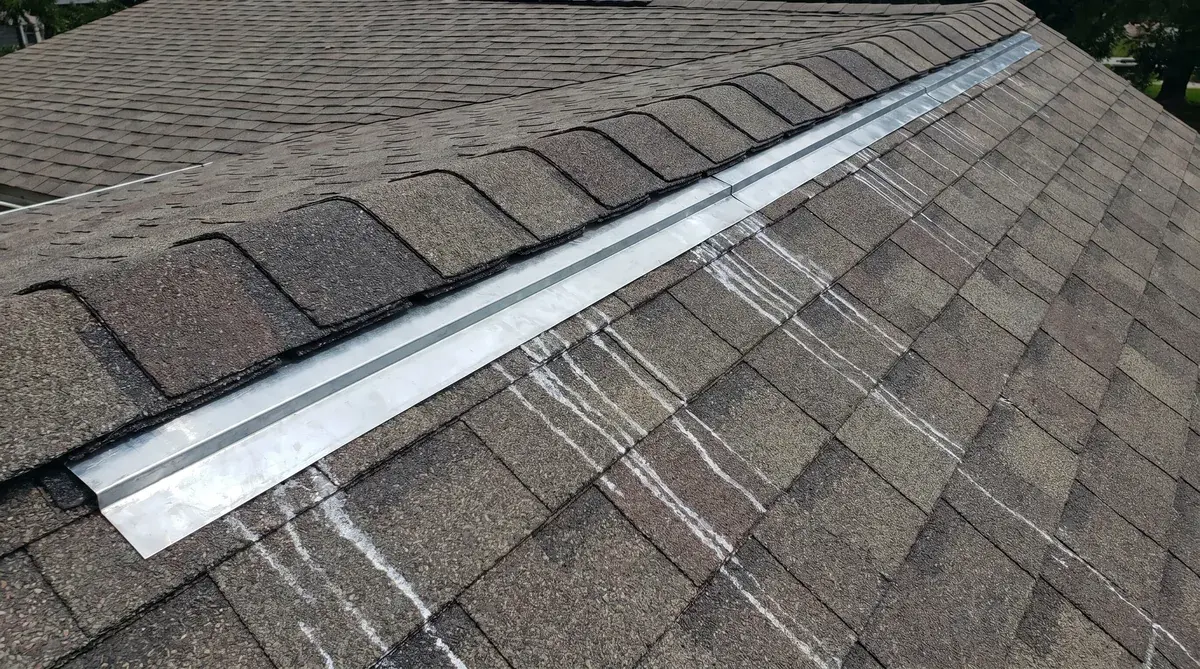 Zinc strips installed along roof ridge with clear view of proper placement under ridge cap shingles